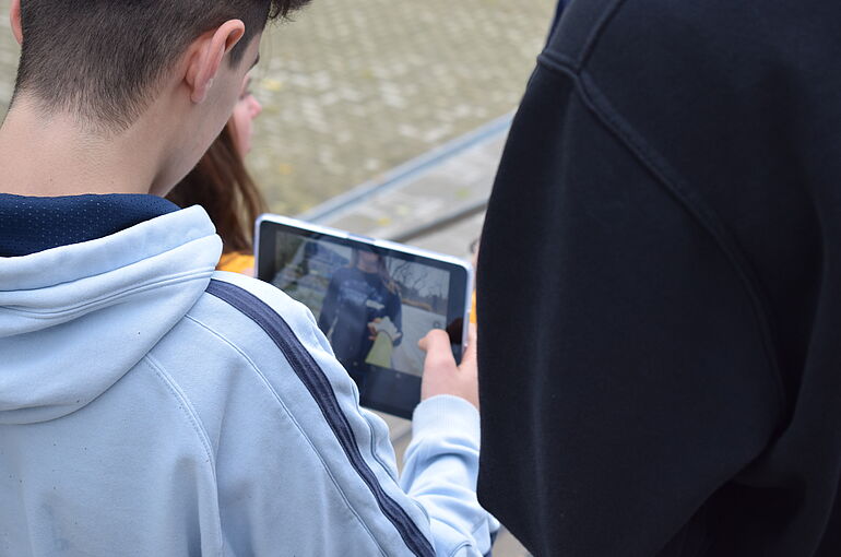 Ein Bild von Hinten, Man sieht einen Jungen der auf sein Ipad guckt.