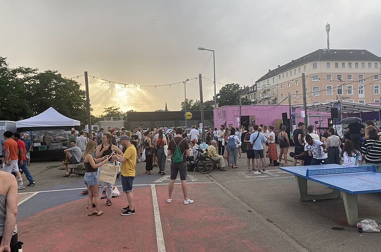 Festivalsituation mit vielen jungen Menschen im Hintergrund, rechts im Bild sieht man eine Tischtennisplatte