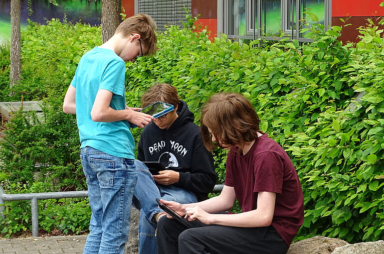 Drei Jungs sitzen draußen und schauen auf ihre Ipads