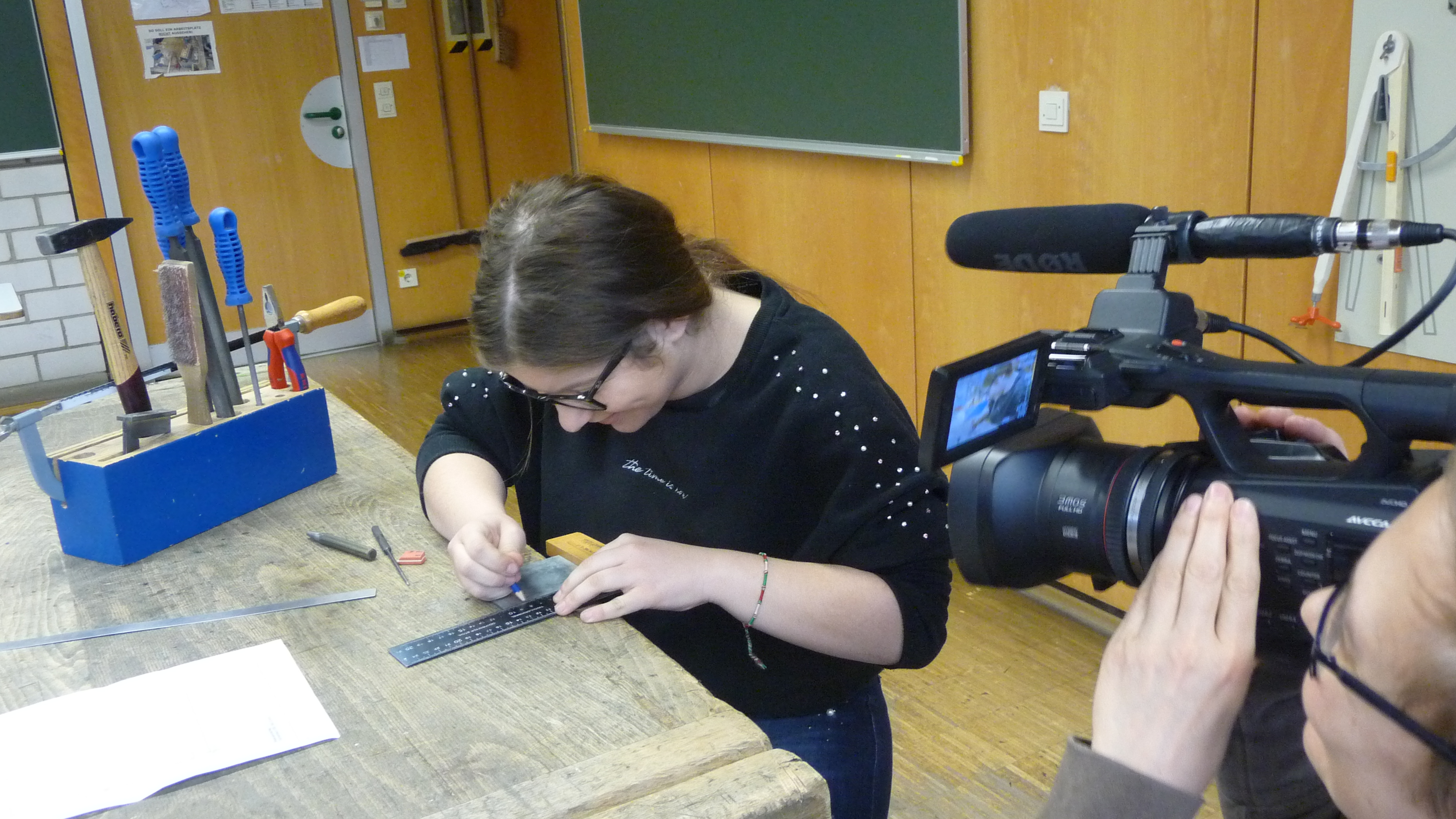 Mädchen an Werkbank arbeitet und wird gefilmt.