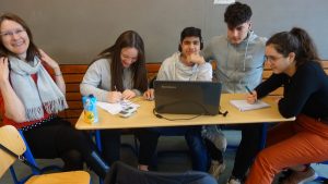 Bild: Eine Grupppe sitzt um einen Tisch. Dabei ein Laptop, ein Aufnahmegerät, Kopfhörer, etwas zu Schreiben und lachende Gesichter