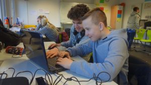 Bild: Zwei Teilnehmer sitzen gemeinsam mit Kopfhörern an einem laptop und schneiden grinsend ihre Aufnahmen zu einem Beitrag zusammen.