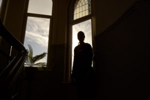 Bild: Foto mit gegenlicht. Der Umriss einer Frau und einer Palm vor einem alten Rundbogenfenster