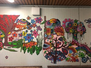 Bild: Ein Schulgang mit betonwänden, die nun von bunten Elefanten, Bäumen, einem Tiger und einem Tukan