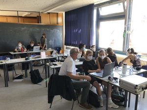 Die ganze Klasse mit Mundschutz aber sehr geschäftig im Klasenraum an vielen Laptops im Schaffensprozess