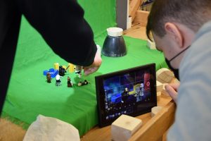 Teilnehmende nehmen mit einem iPad und Lego Figuren vor einem Green Screen einen Stop-Motion-Film auf