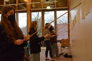 Teilnehmende zeichnen mit Stiften an einmeterlangen Stäben