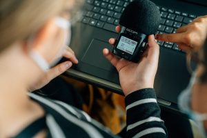 Eine Teilnehmer*in hält ein Zoom Aufnahmegerät in der Hand. Im Hintergrund steht auch schon der Laptop bereit.