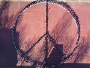 Die Schüler*innen einer Schule formen ein großes Peace Zeichen auf dem Sportplatz.