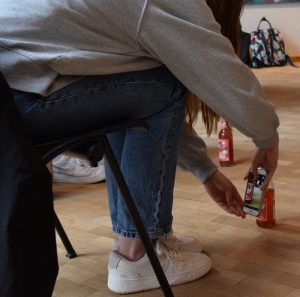 Jugendliche sitzt auf einem Stuhl und Fotografiert mit ihrem Handy den Boden und ihre Flasche
