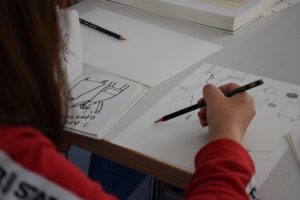 Ein Mädchen zeichnet mit einem Bleistift Skizzen auf ein Papier