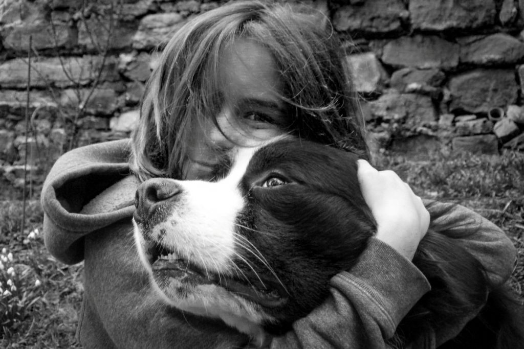 Bild der Gewinnerin- sie sitzt kuschelnd mit ihrem Hund vor einer Mauer, das Bild ist in Schwarz/Weiß