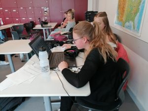 eine Klasse arbeitet mit laptops und Kopfhörern bei einem radio projekt. Wobei die Gruppe im vordergrund richtig vertieft in die Arbeit wirkt.