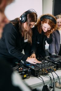 Zwei Teilnehmende aus dem FILNTA DJ Workshop legen gemeinsam auf dem Mischpult auf - mit Begeisterung in den Gesichtern und und professioneller Gestik.