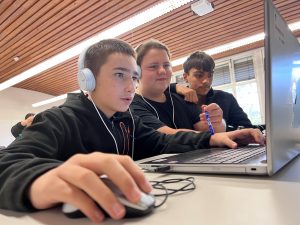 Drei Schüler*innen arbeiten mit Spaß und im Team am Laptop und bearbeiten die frisch aufgemommenen Soundfiles.
