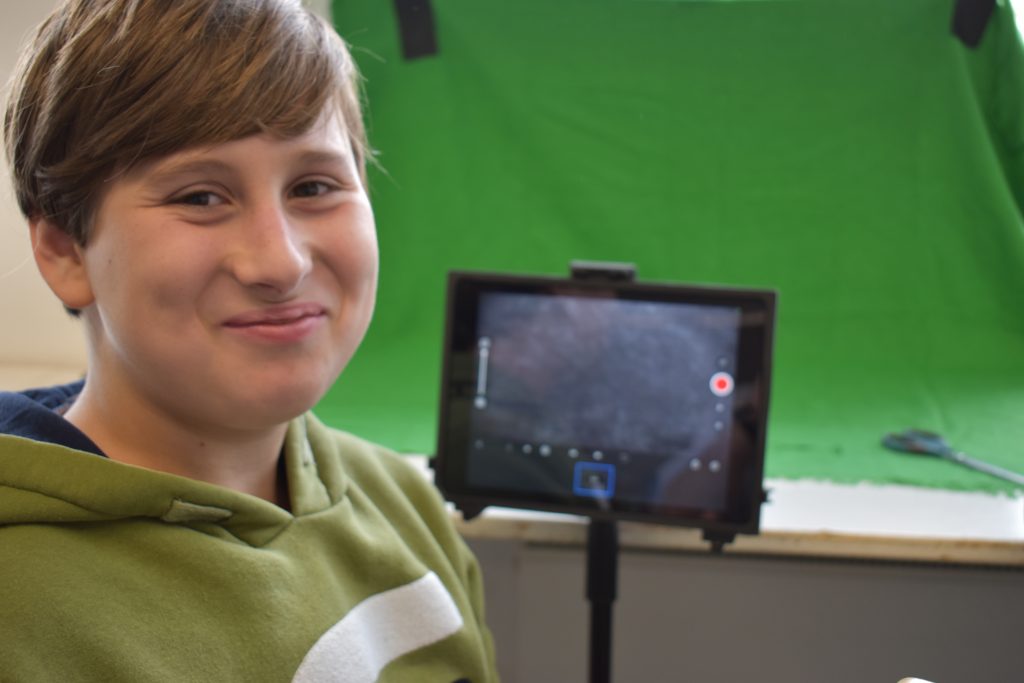 Kind lächelt, im Hintergrund Greenscreen und Tablet