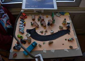 Tisch mit Spielzeugautos und Figuren, der mit einem Tablet gefilmt wird