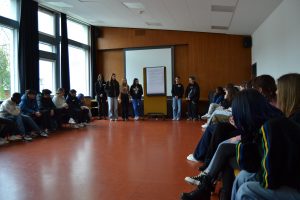 Jugendliche sitzen im Kreis in einem Saal, vonre präsentiert eine Gruppe ihr Projekt