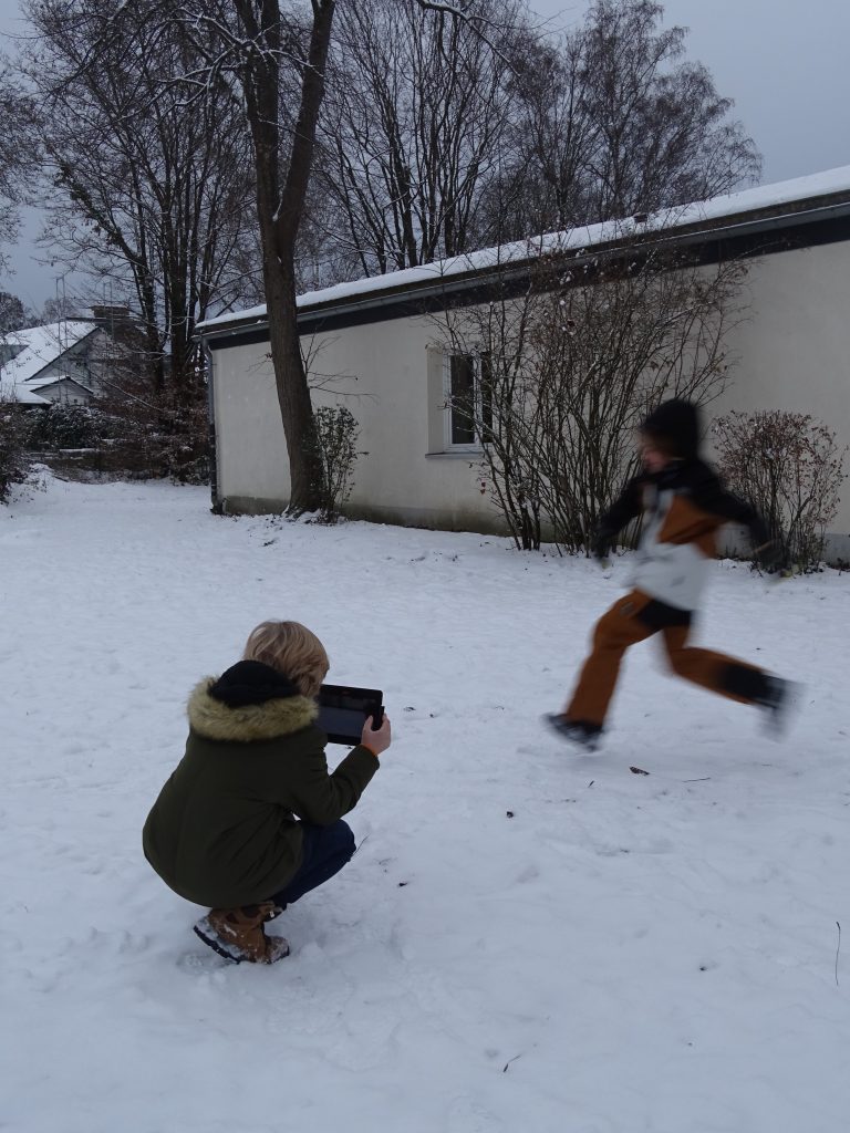 Auf dem Foto sind zwei Schüler im Schnee zu sehen, wie sie gerade eine Szene aufnehmen.