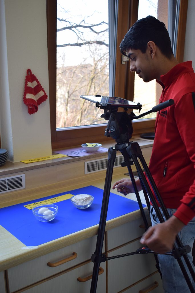 Ein Schüler filmt mit einem Stativ und Tablet ein Video mit Mehl und Eiern.