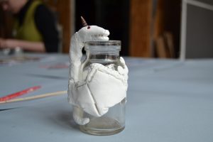 Ein Fabelwesen aus Modelliermasse schlängelt sich um ein Glas