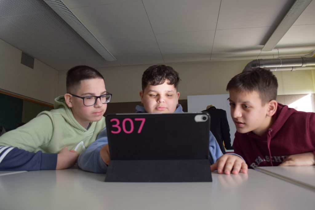 Drei Schüler sitzen im Klassenzimmer vor einem Tablet.