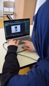 Ein Mädchen mit Hijab bearbeitet ein Bild an einem Laptop