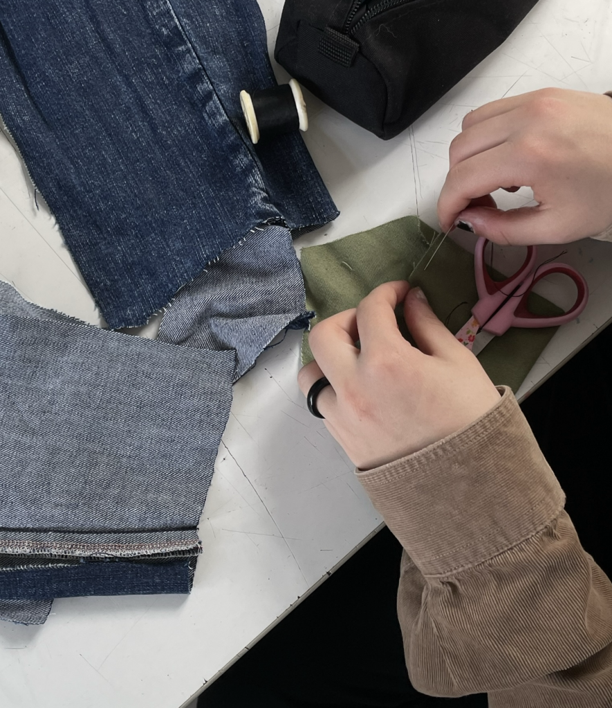 Ein Arbeitsplatz von oben. Eine zurecht geschnittene Jeanshose, eine Schere und Faden lassen erahnen, dass daraus gleich etwas Neues entsteht. 