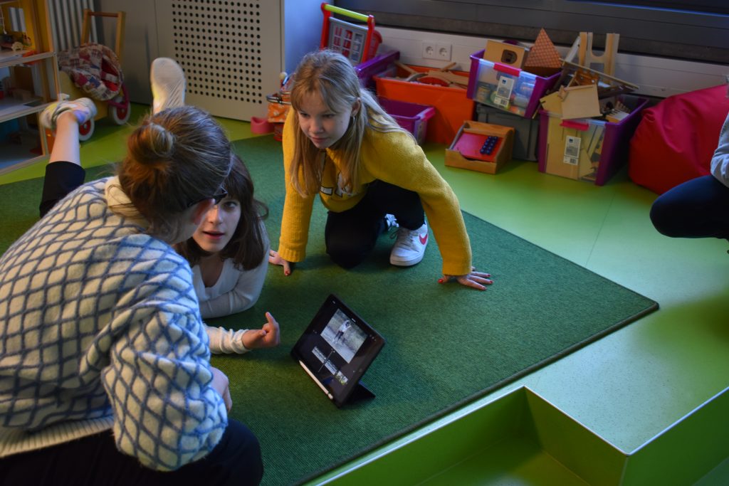 Drei Mädchen sitzen um ein Tablet herum und diskutieren miteinander.