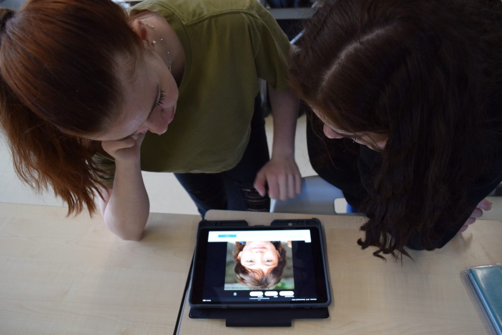 Zwei Mädchen stehen um ein Tablet herum, auf welchem ein Foto eines Kindes zu sehen ist.