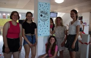 Die vier Kulturstarterinnen und ihrer lehrerin stehen stolz um die bemalte Säule im Foyer der Schule