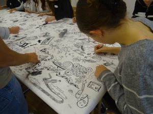 Jugendliche malen auf einem grpßen weißen Blatt mit Kohle