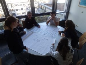 Eine Gruppe plant um einen runden Tisch Herum und sammelt Ideen gemeinsam auf einem Plakat
