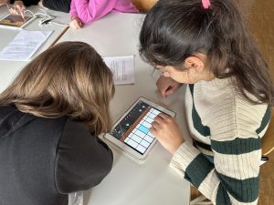 Zwei Schülerinnen beugen sich über ein Tablet, auf dem ein Sundprogramm geöffnet ist.