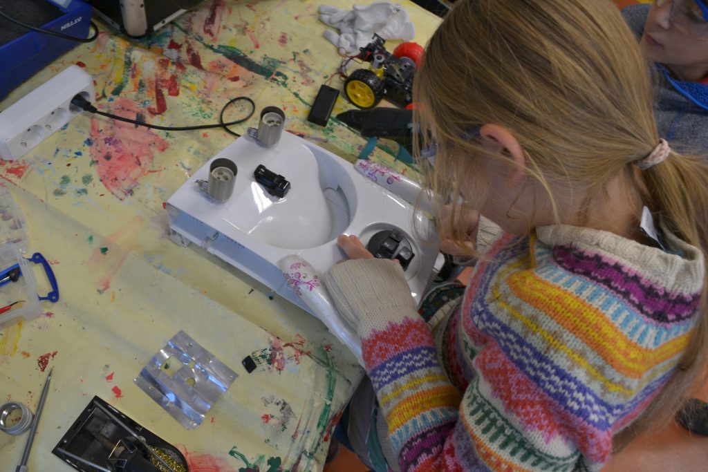 Grundschulkind beugt sich über ein aus Schrott gebauten Kunstroboter