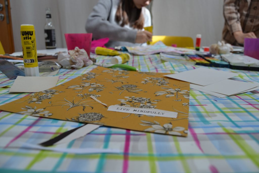 Ein kreativer Besteltisch voller verschiedener Materialien. Im Fokus der Schriftzug "life mindfully" auf einem buten Stück Papier