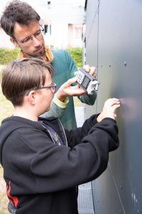 eine Person kratzt an einer wand eine zweite Person hält ein Aufnahmegerät ganz nah daneben