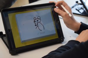 Auf einem Tabletbildschirm ist ein handgezeichneter Bär zu sehen, darunter der Text "bear".