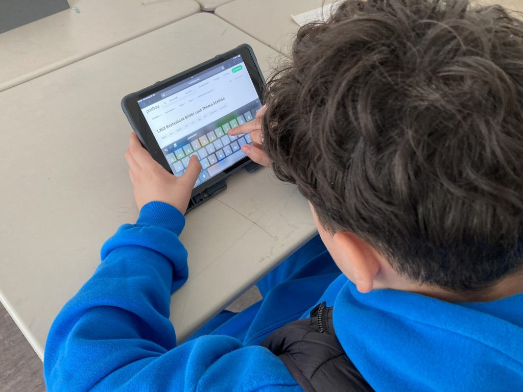 Jugendlicher tippt auf einem Tablet, Blick über seine Schulter