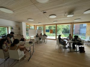 um drei Tische herum sitzen Grüppchen fleißig schreibender Schülerinnen in einem Klassenraum