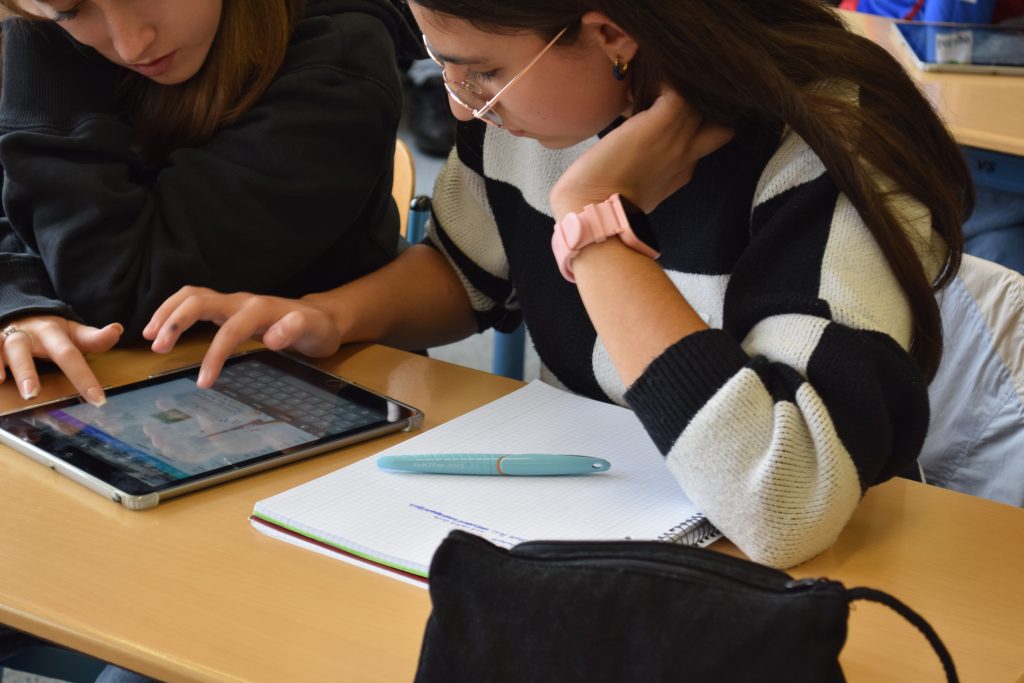 Zwei Jugendliche schauen auf ein Tablet das vor ihnen auf dem Tisch liegt und tippen darauf.
