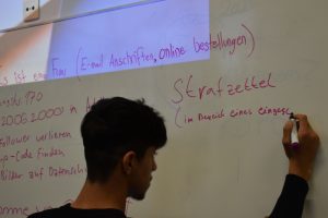 Jugendlicher steht vor Whiteboard und schreibt Stichworte darauf.