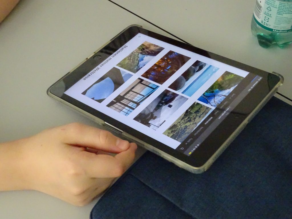 Ein Tablet ist zu sehen mit Urlaubsbildern auf dem Bildschirm, daneben eine Hand.