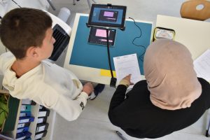 Man blickt von oben auf zwei Jugendliche die wiederum ein Tablet in einer Halterung eingespannt haben, um von oben auf den Tisch zu filmen.