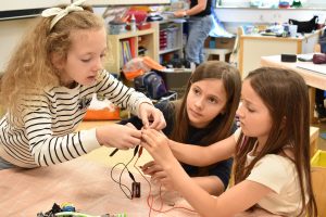 drei Mädchen verbinden Kabel mit einer Batterie und einer Glühbirne.