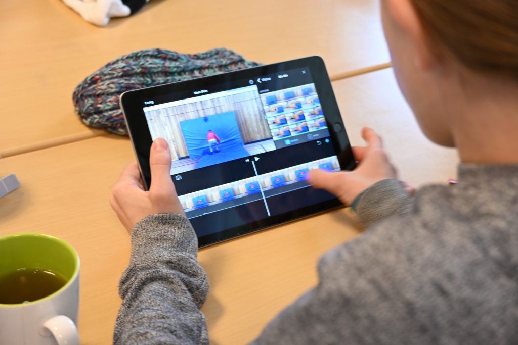 Blick über die Schulter einer Schülerin, die an einem Tablet ein Video bearbeitet (Schnitt).
