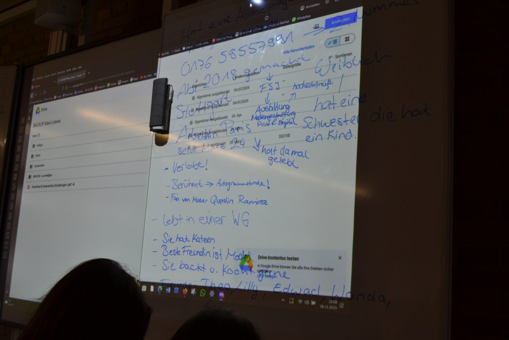 Ein Smartboard ist zu sehen mit gesammelten Hinweisen, die Handschriftlich notiert wurden. Beispielsweise "lebt in einer WG".