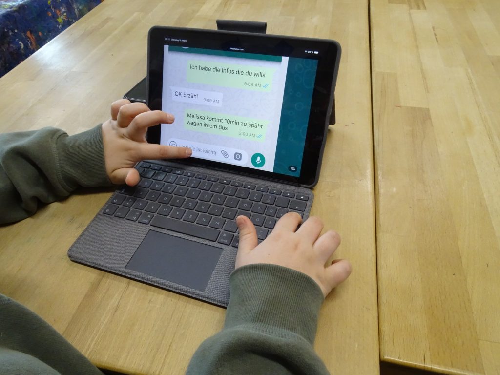 Zu sehen ist ein Tablet, aufgestellt auf einem Tisch, zu sehen ist ein fiktiver Chatverlauf.