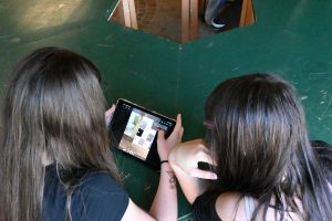 Zwei Schülerinnen schauen gemeinsam auf ein Tablet, es sind nur ihre Hinterköpfe mit langen Haaren zu sehen.