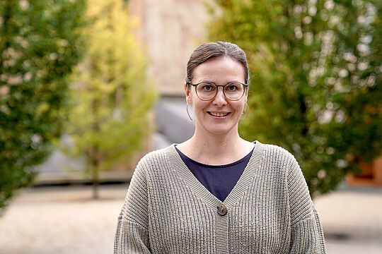 Eine Frau mit Zopf und Brille lächelt in die Kamera.